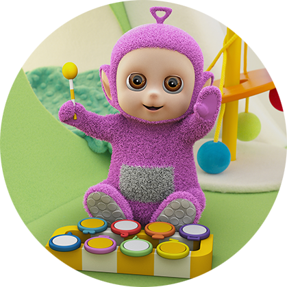 A light purple character, with a round beige face, is sitting on a green floor playing a musical instrument.